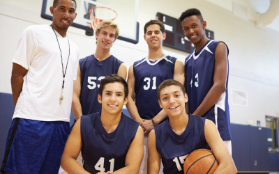 High school basketball team poses in gym with coach