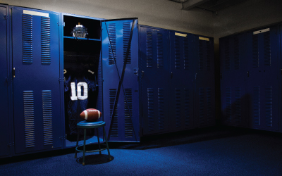 Blue locker room with open locker holding a football jersey, football, and helmet