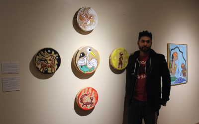 Mike Cywink standing next to 5 drums he painted with clan animals, representing different teachings and roles and responsibilties
